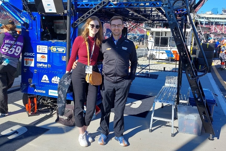 A man and a woman standing in the pit area at a stockcar track. 