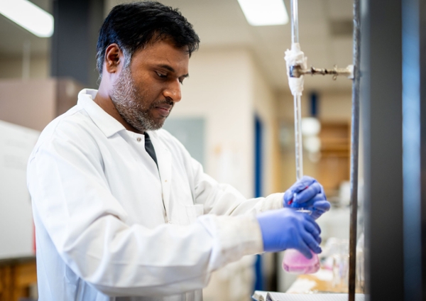 Male student in a lab looking at a beaker filled with chemicals.