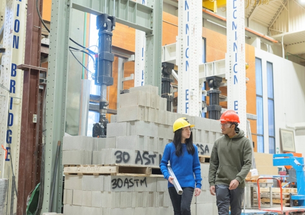 Two students walking in the structures lab wearing hardhats.