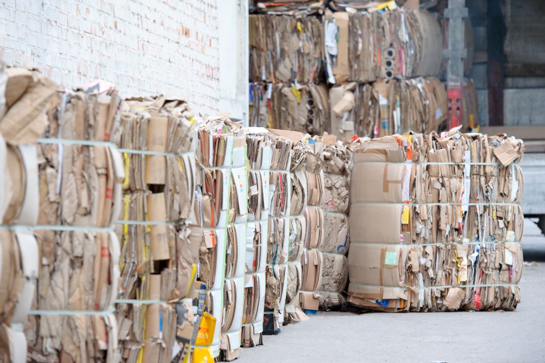 Large bundles of recycled paper sit on pallets in a recycling facility