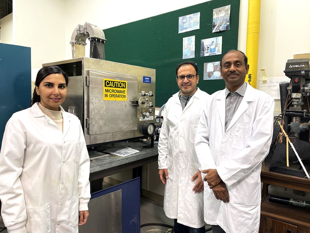 Three researchers in white lab coats stand in front of lab equipment