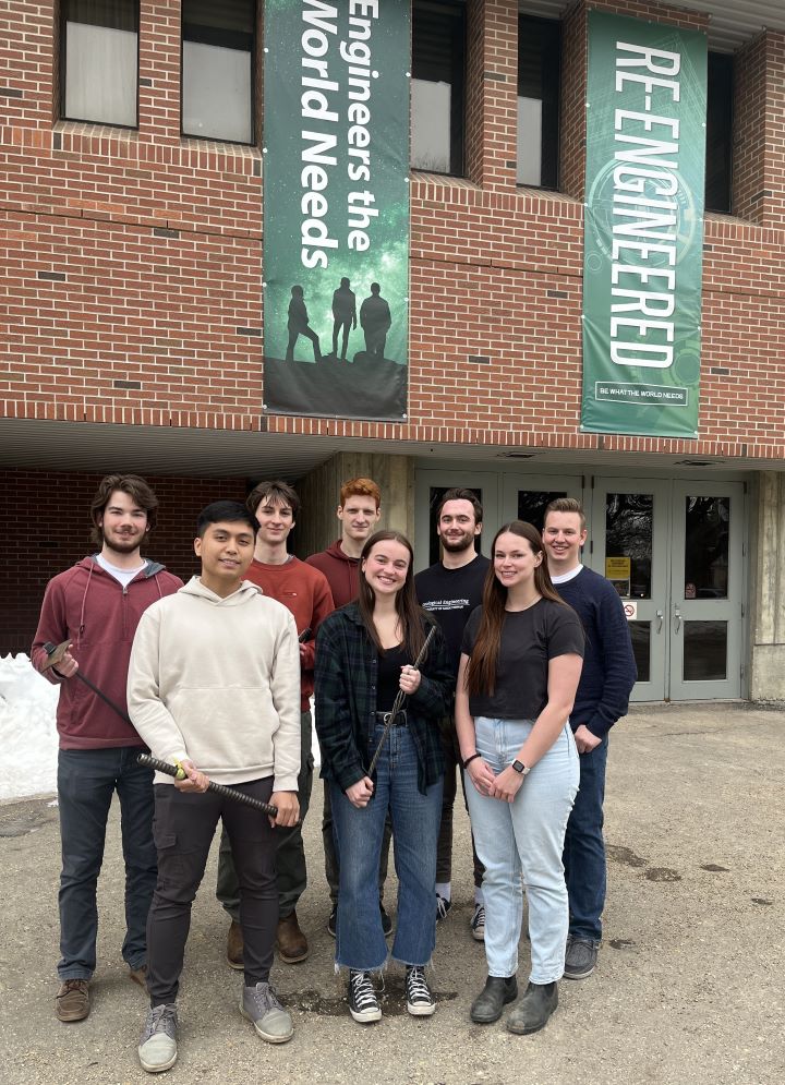 A group of eight female and male engineering students stand in front of the USask College of Engineering. 